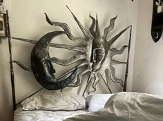 a metal sun and moon head on a wall above a bed with white linens