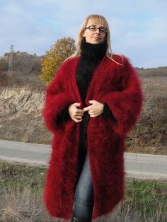 a woman standing in the grass wearing a red fur coat and black turtle neck sweater