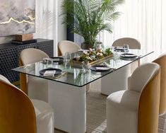 a glass table with chairs around it in front of a painting and plants on the wall