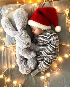 a baby wearing a santa hat sleeping next to a stuffed animal