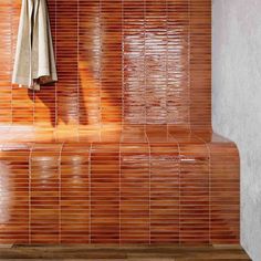 an orange tiled wall in a bathroom next to a towel rack and wooden flooring