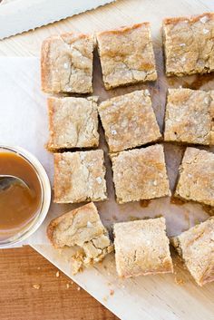 several squares of food sitting on top of a cutting board next to a bowl of sauce