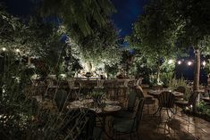 an outdoor dining area at night with tables and chairs set up in the middle, surrounded by greenery