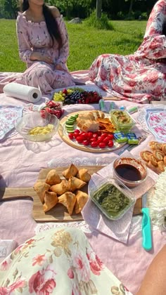 two women sitting at a picnic table with food on it