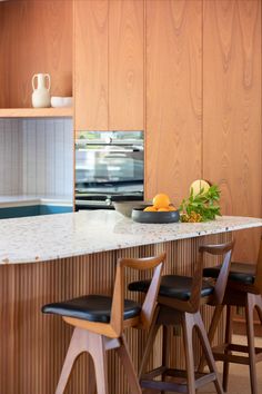 a kitchen with wooden cabinets and black leather bar stools next to an island counter