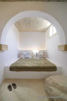 a bed sitting in the middle of a room under a window next to a pair of shoes