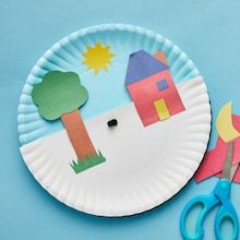 a paper plate with cut out houses and trees on it next to scissors, glue and construction paper