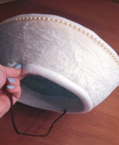 a woman's hand holding a white hat on top of a wooden table