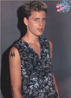 a young man with a bat tattoo on his left arm and chest, standing in front of a gray background