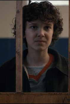 a young boy looks out from behind the bars in a jail cell, looking at the camera