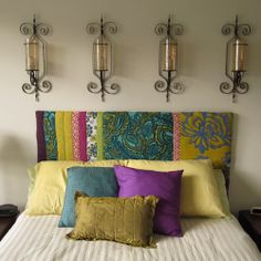 a bed topped with lots of pillows next to two wall sconces on either side of it