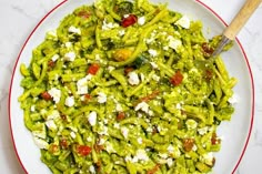 a white plate topped with green pasta covered in feta cheese and sauce next to a wooden spoon