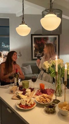 two women sitting at a table with food and wine