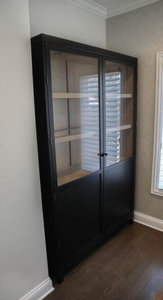 an empty room with a large black cabinet and window in the corner that has shutters on both sides