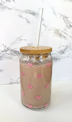 a glass jar with a straw in it and hearts on the lid next to a marble wall