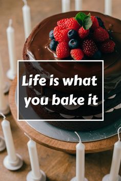 a chocolate cake with strawberries and blueberries on top sits in front of candles