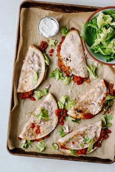 an open faced sandwich with lettuce, tomato and sauce on it next to a bowl of salad