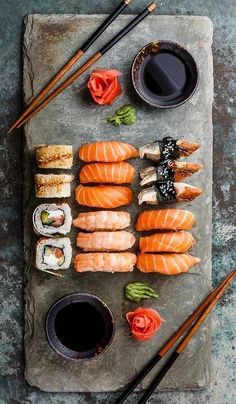 sushi and chopsticks are laid out on a slate board