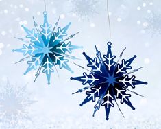 two blue snowflakes hanging from strings on a white background with snow flakes