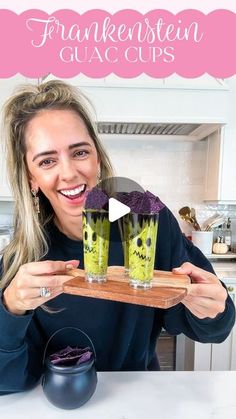 a woman holding up two glasses filled with green liquid and purple stuff in front of her face