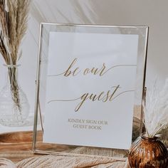 a sign that says be our guest next to a vase with dried grass in it