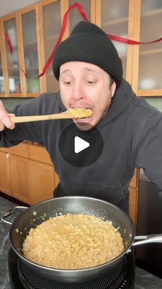 a man in a beanie is eating cereal from a frying pan on the stove