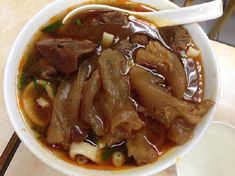 a white bowl filled with meat and vegetables next to chopsticks on a table