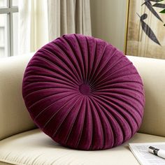 a purple round pillow sitting on top of a couch next to a pen and paper