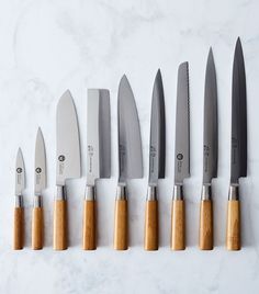 six knives lined up in a row on a marble counter top with wooden handles and blades