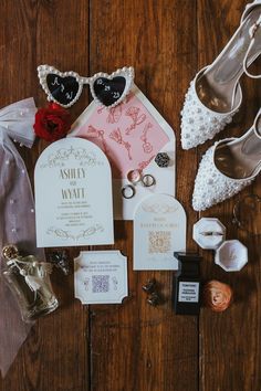 wedding stationery and accessories laid out on a wooden floor with bride's shoes