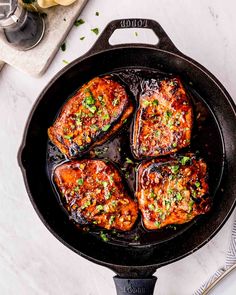 four cooked meats in a skillet on a white table with utensils