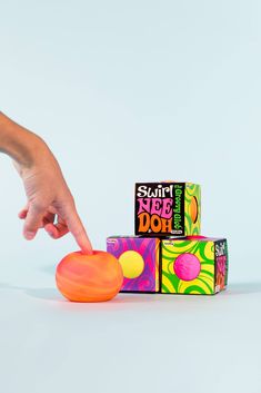 a hand reaching for an orange frisbee on top of three colorful cubes