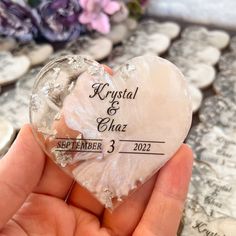 a person holding a crystal heart with the date printed on it in front of flowers