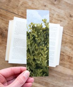 a hand holding an open book with green leaves on it and a page in the background