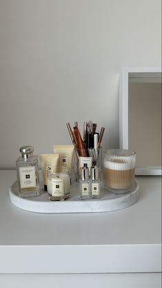 an assortment of candles and personal care items on a white countertop in front of a mirror