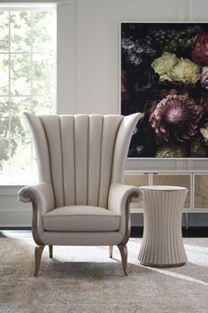 an elegant chair and side table in front of a large flowered painting on the wall