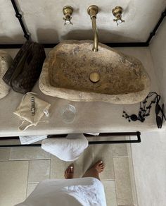 a person standing next to a stone sink in a room with white walls and tile flooring