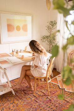 a woman sitting at a desk in front of a mirror and painting on the wall