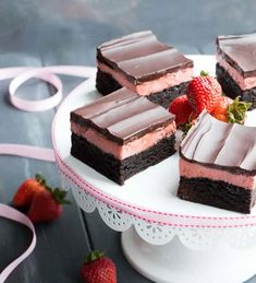 four pieces of chocolate cake on a white plate with strawberries and pink ribbon around the edge