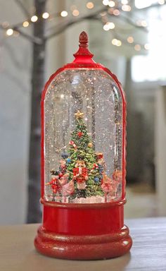 a snow globe with a christmas tree inside on top of a table in front of some lights