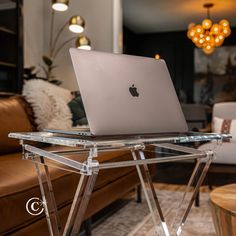 an apple laptop sitting on top of a clear table next to a couch and coffee table