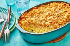 a casserole dish on a blue table with silverware and water in the background