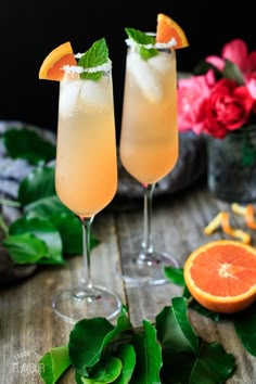 two glasses filled with drinks sitting on top of a table next to an orange slice