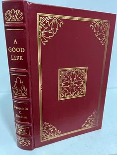 a red book with gold trim on the front and back cover, sitting on a white surface