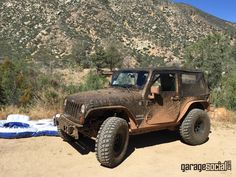 an old jeep is parked in the sand near a mountain range with trees and bushes