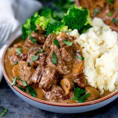 a bowl filled with meat, mushrooms and broccoli on top of mashed potatoes