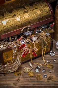 an old trunk filled with lots of gold and silver jewelry sitting on top of a wooden table