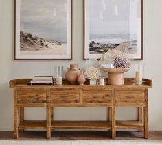 two framed pictures hang above a wooden table with vases and books on the top