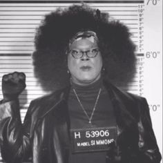 a woman with an afro is holding her fist up in front of a mug shot