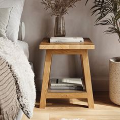 a small wooden table sitting next to a bed with pillows and blankets on top of it